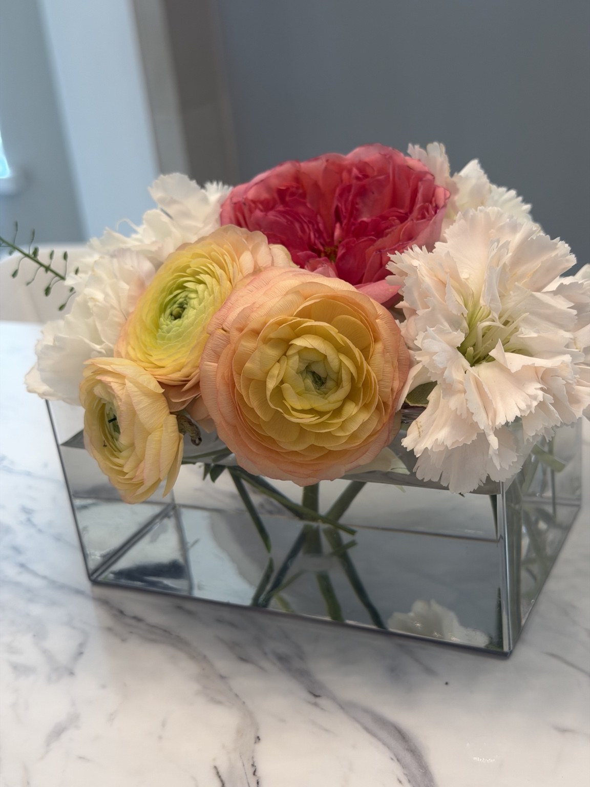 Peach and yellow ranunculus floral arrangement in a mirrored container by Petite Petal