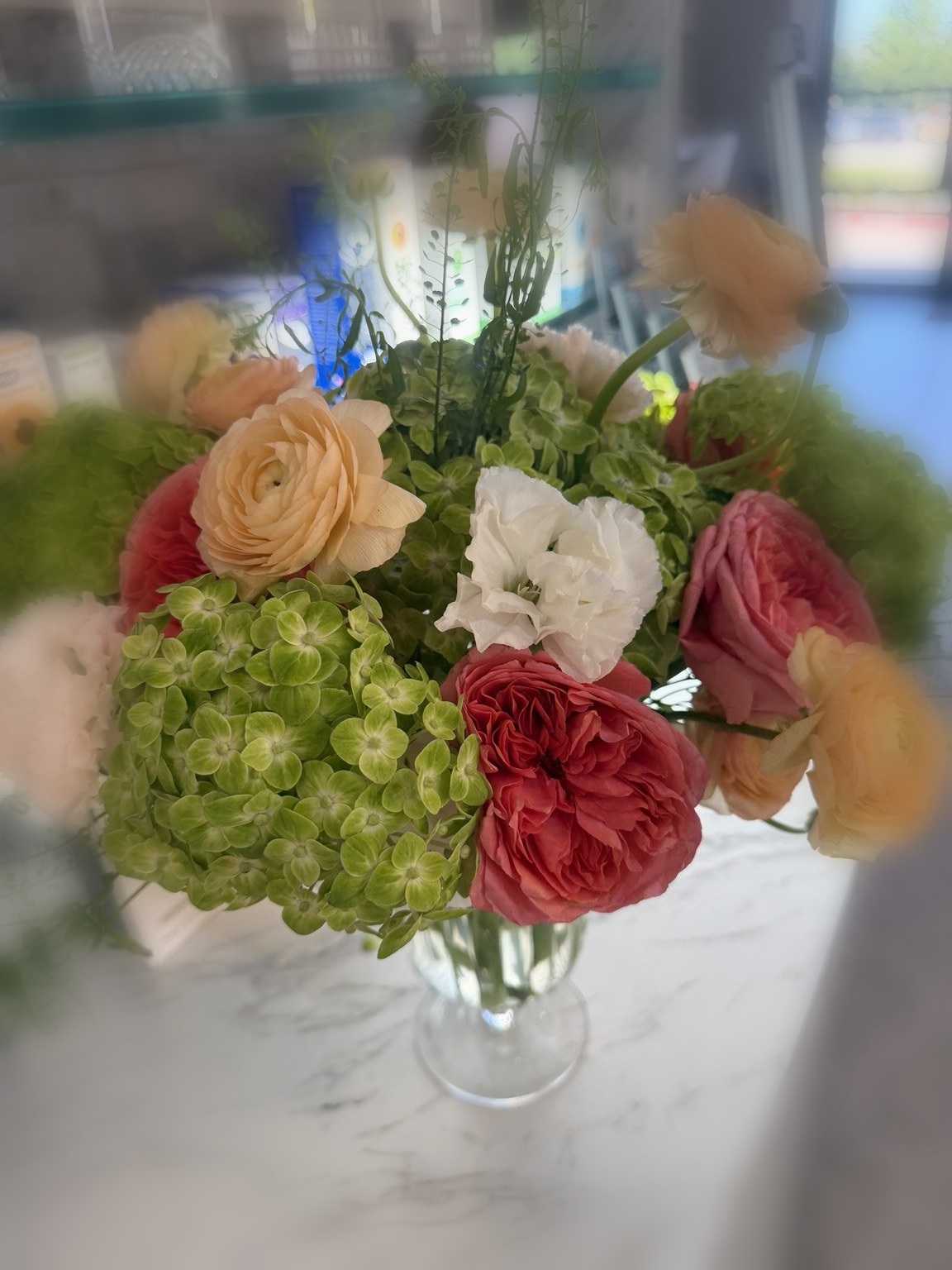 Green hydrangea and peach ranunculus event arrangement with coral roses by Petite Petal